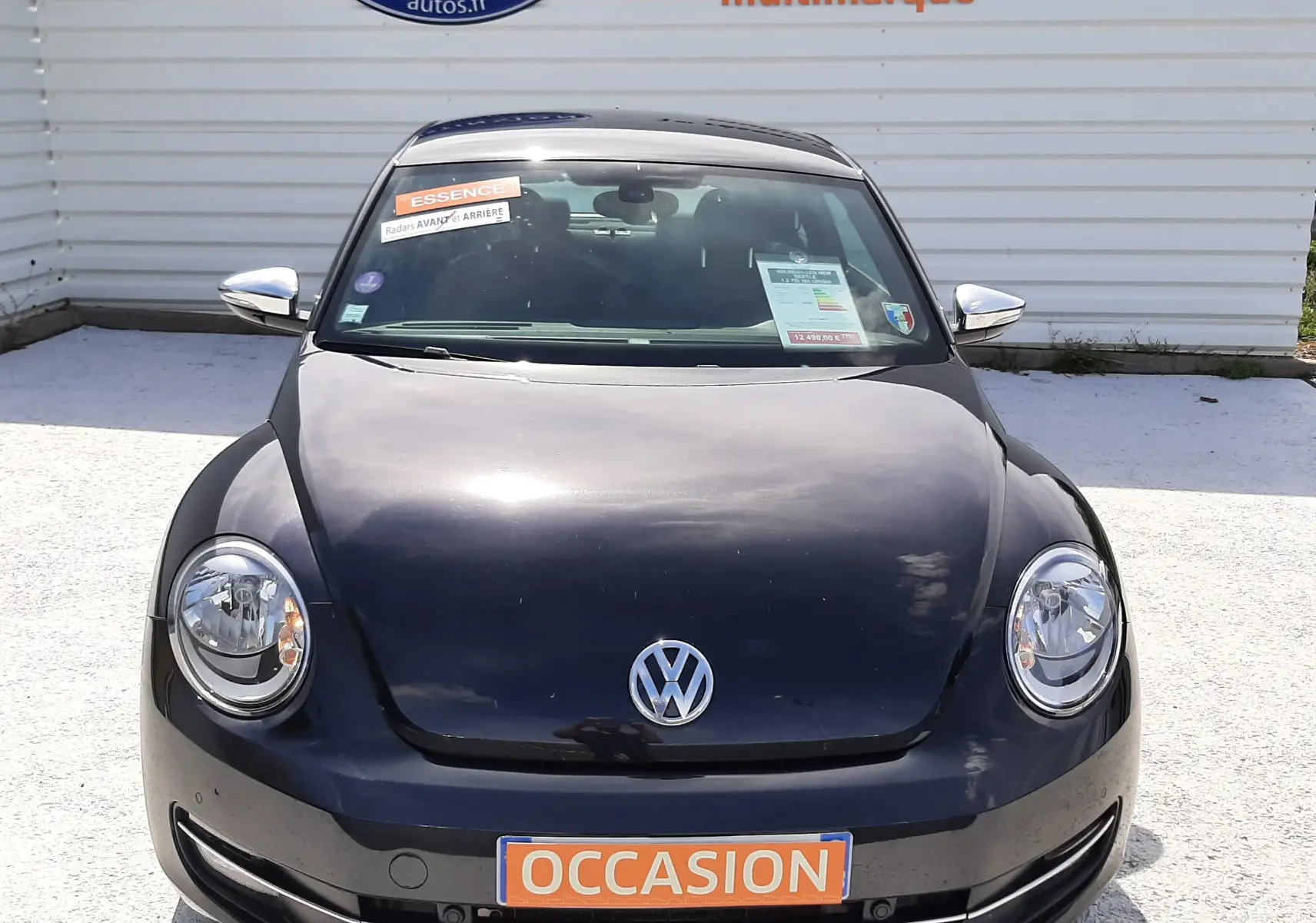 Vue avant d'une Volkswagen New Beetle noire de 2015 avec plaque "OCCASION" et autocollants sur le pare-brise.
