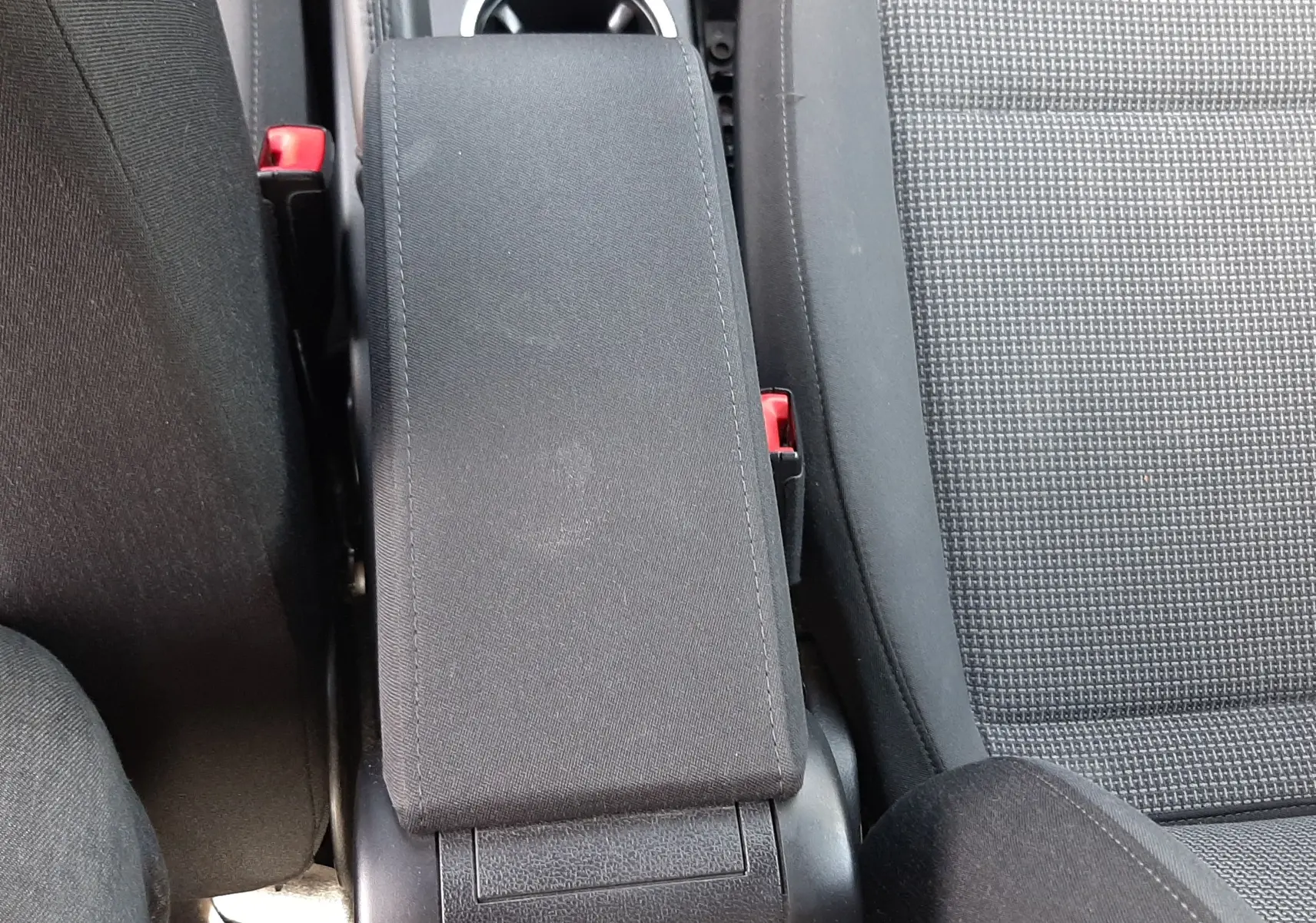 Vue plongeante sur l'accoudoir central noir et les sièges en tissu gris du Volkswagen New Beetle 2015.