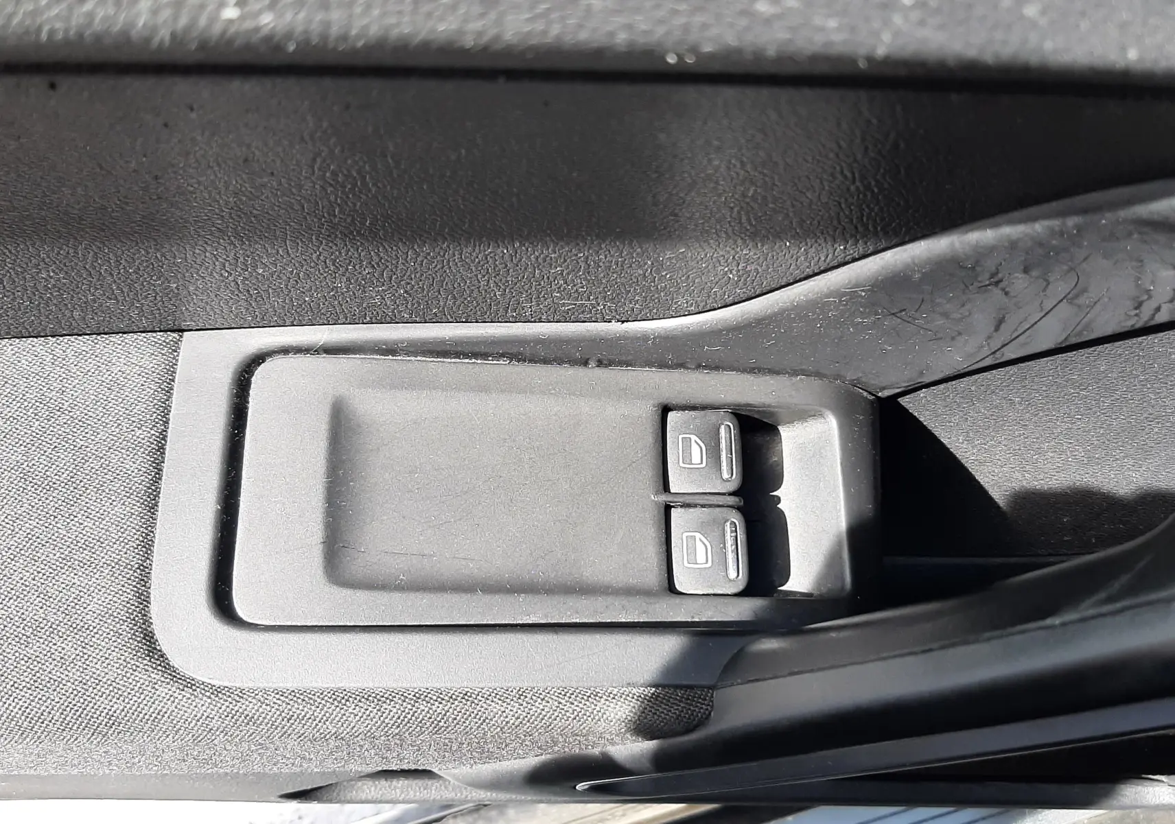 Gros plan sur les commandes électriques des vitres côté conducteur d’un Volkswagen New Beetle noir de 2015.