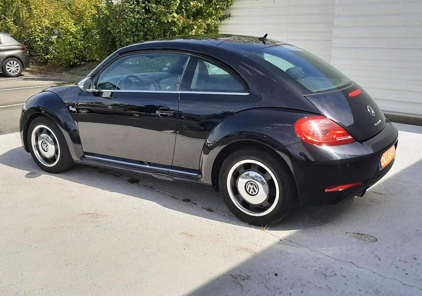 Volkswagen New Beetle noir en vue 3/4 arrière droit, avec jantes d'origine et feux arrière allumés.