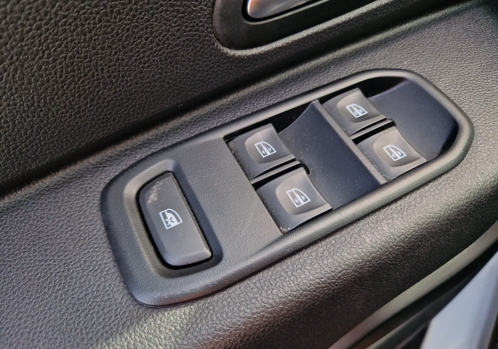 Gros plan sur les commandes de lève-vitres électriques côté conducteur du Dacia Duster 4x4 blanc 2023.