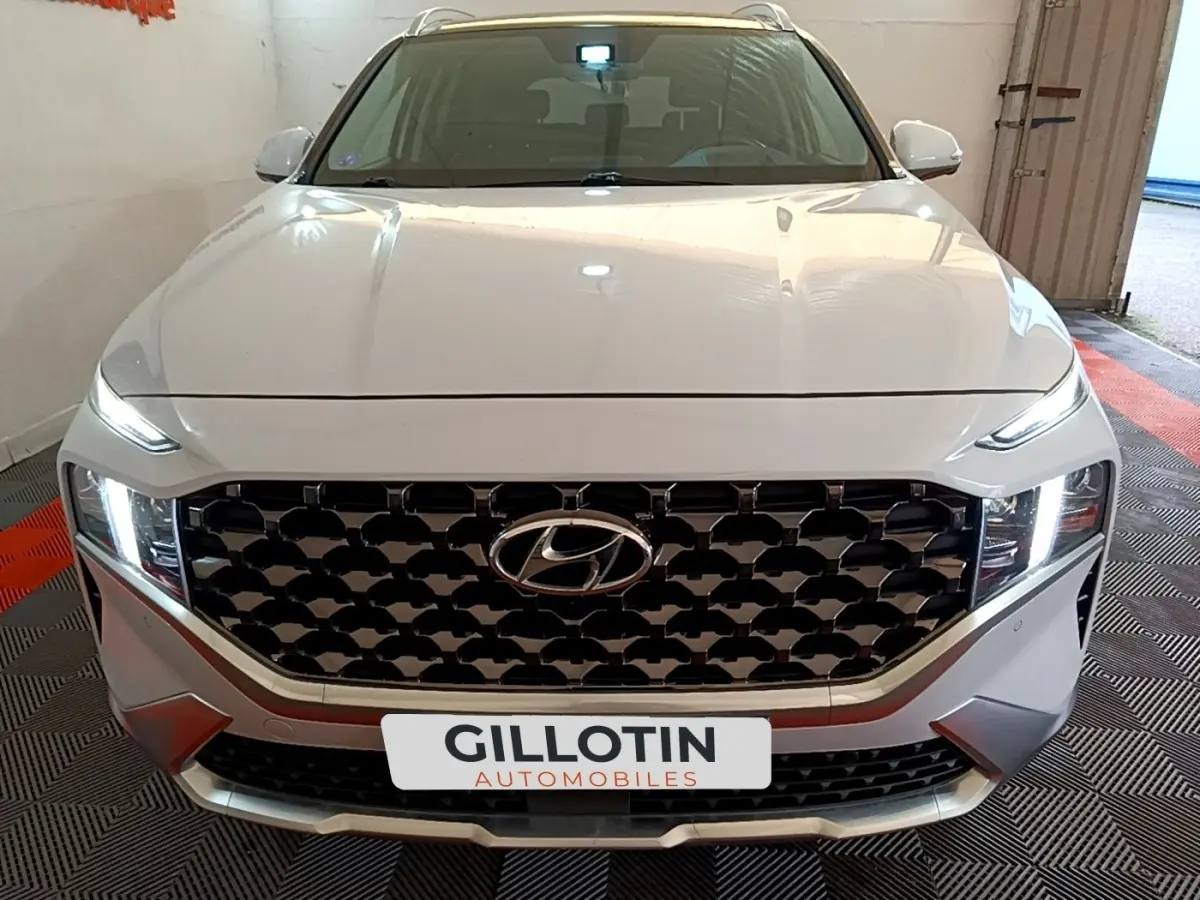 Vue frontale d'un Hyundai Santa Fe blanc avec calandre noire à motifs géométriques et phares LED allumés.