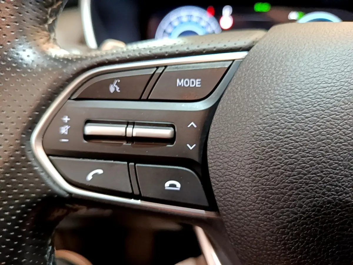 Gros plan sur les commandes du volant côté gauche du Hyundai Santa Fe blanc 2022, boutons mode et téléphone visibles.