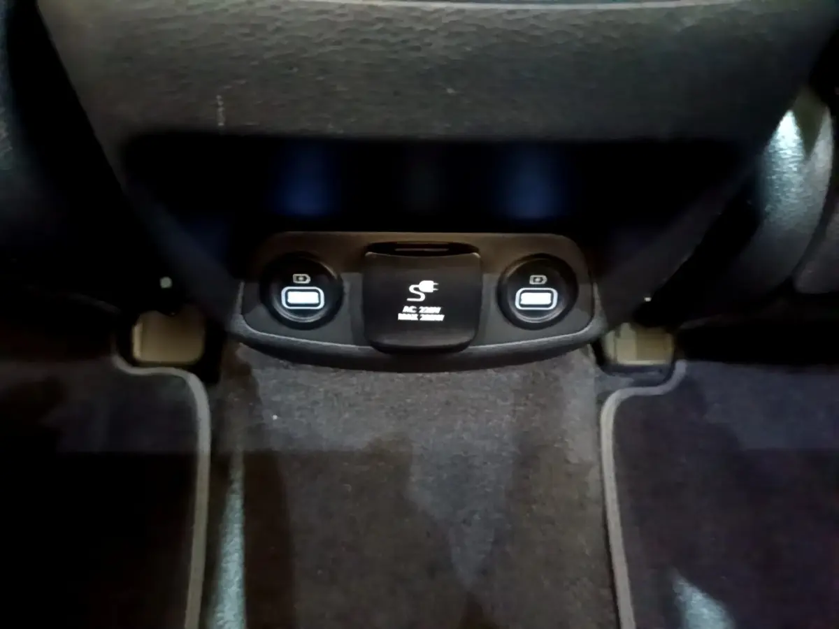 Prise de courant 220V et ports USB arrière sur tapis noir dans l'habitacle du Hyundai Santa Fe blanc 2022.