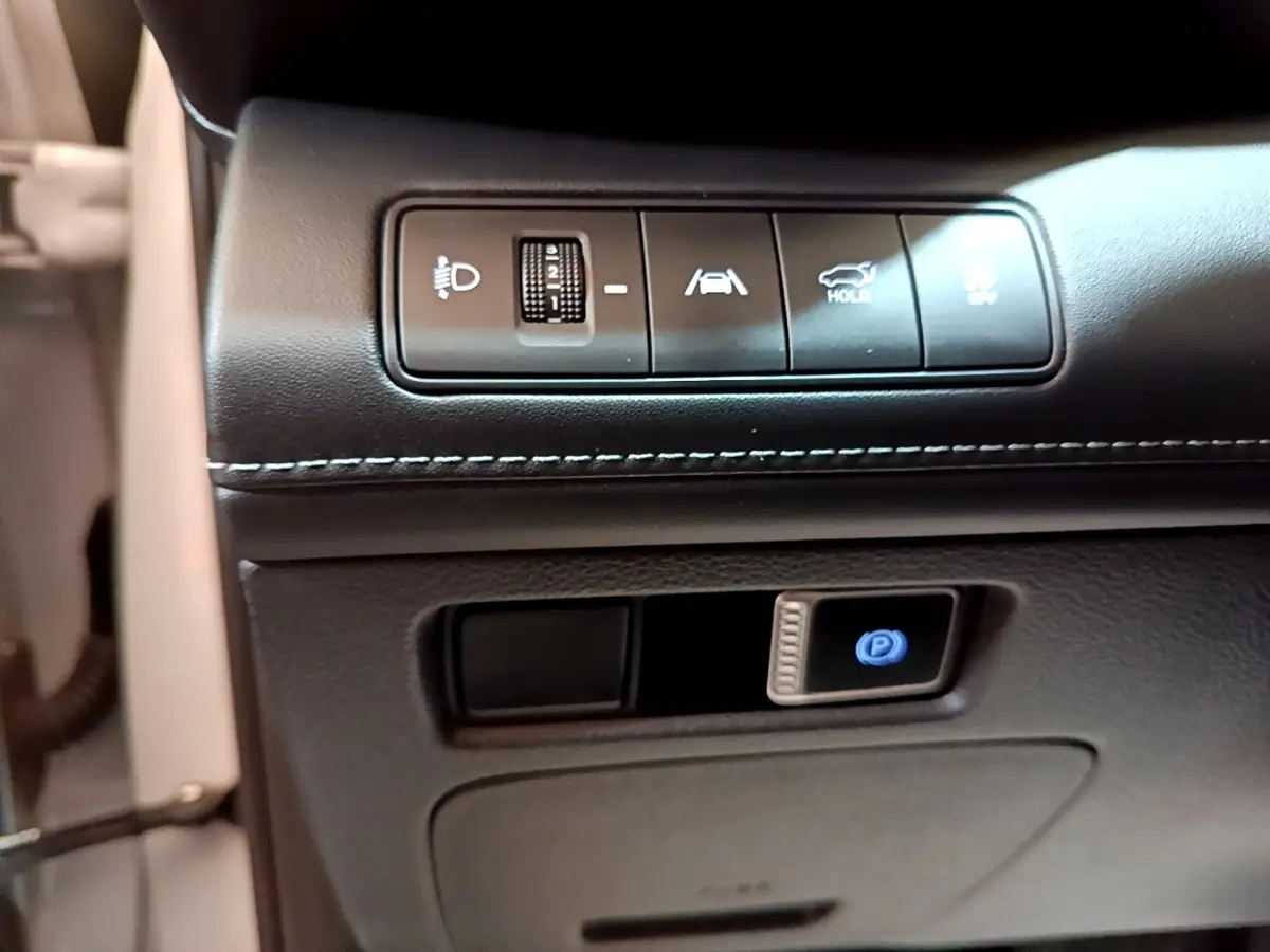 Gros plan sur les commandes de réglage des phares, assistance au maintien de voie et frein de parking électrique du Hyundai Santa Fe blanc 2022.