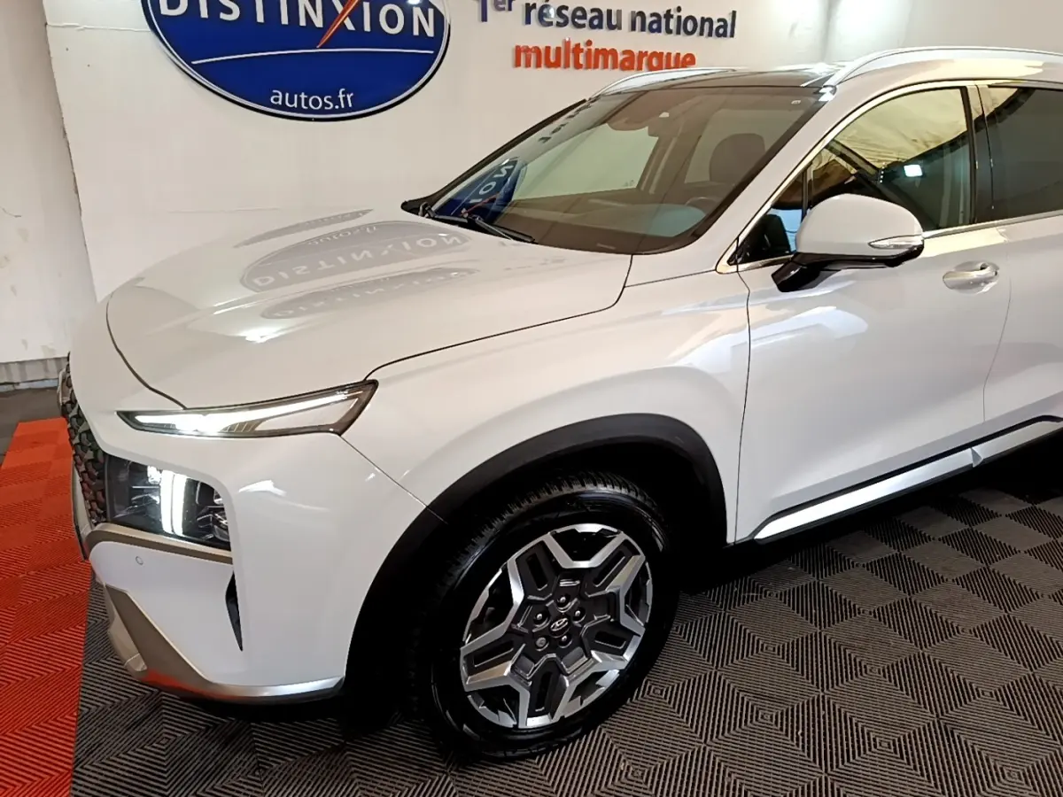 Vue 3/4 avant droit d'un Hyundai Santa Fe blanc avec jantes alliage et feux LED distinctifs en intérieur showroom.