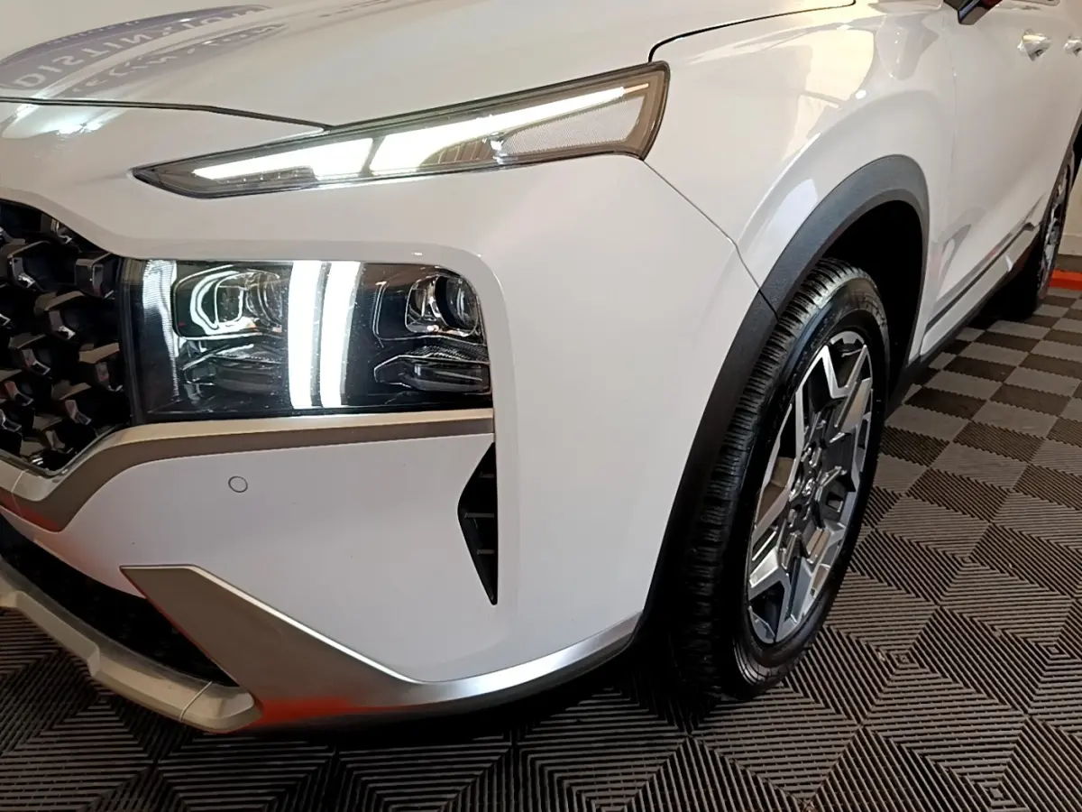 Gros plan sur l'avant droit blanc du Hyundai Santa Fe 2022, mettant en valeur les phares LED et la jante alliage.