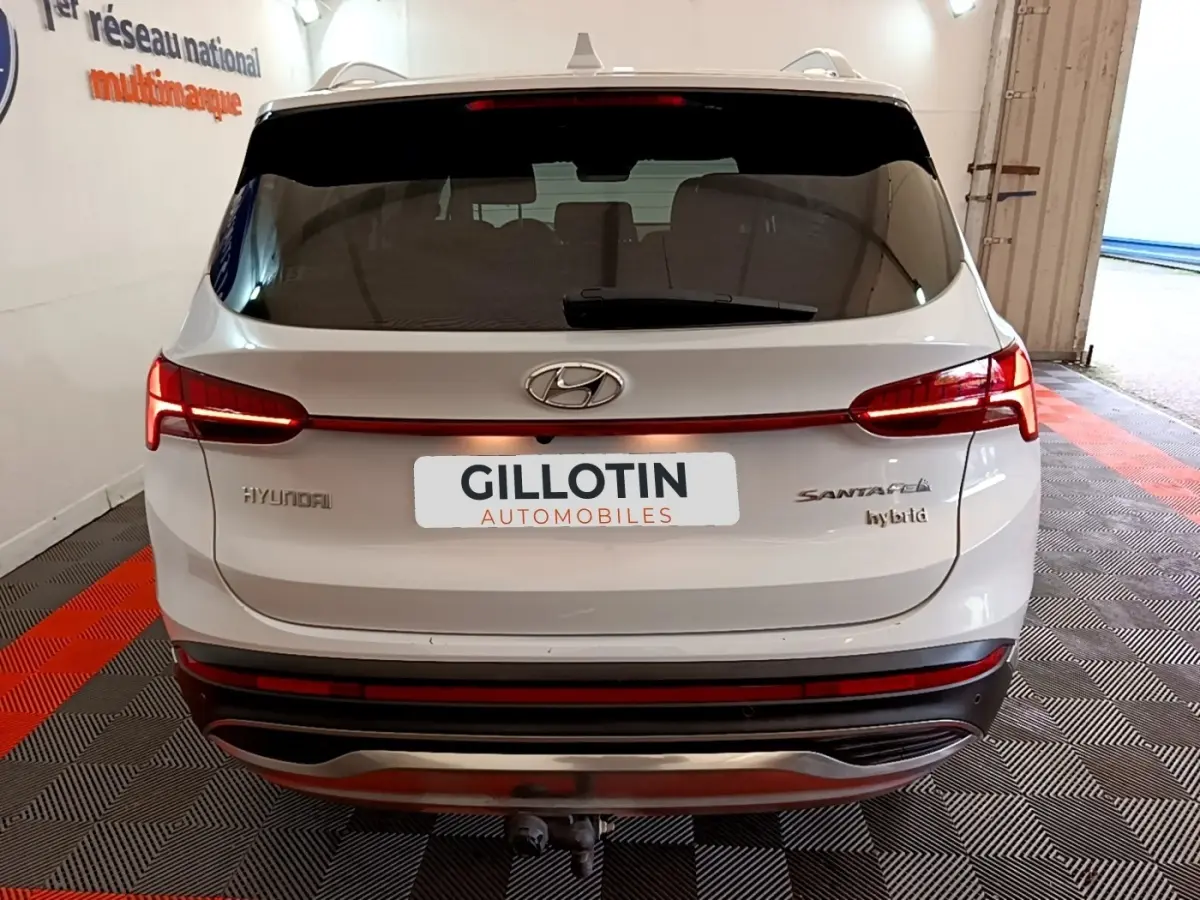 Vue arrière d'un Hyundai Santa Fe blanc hybride avec feux LED reliés par une bande lumineuse rouge.