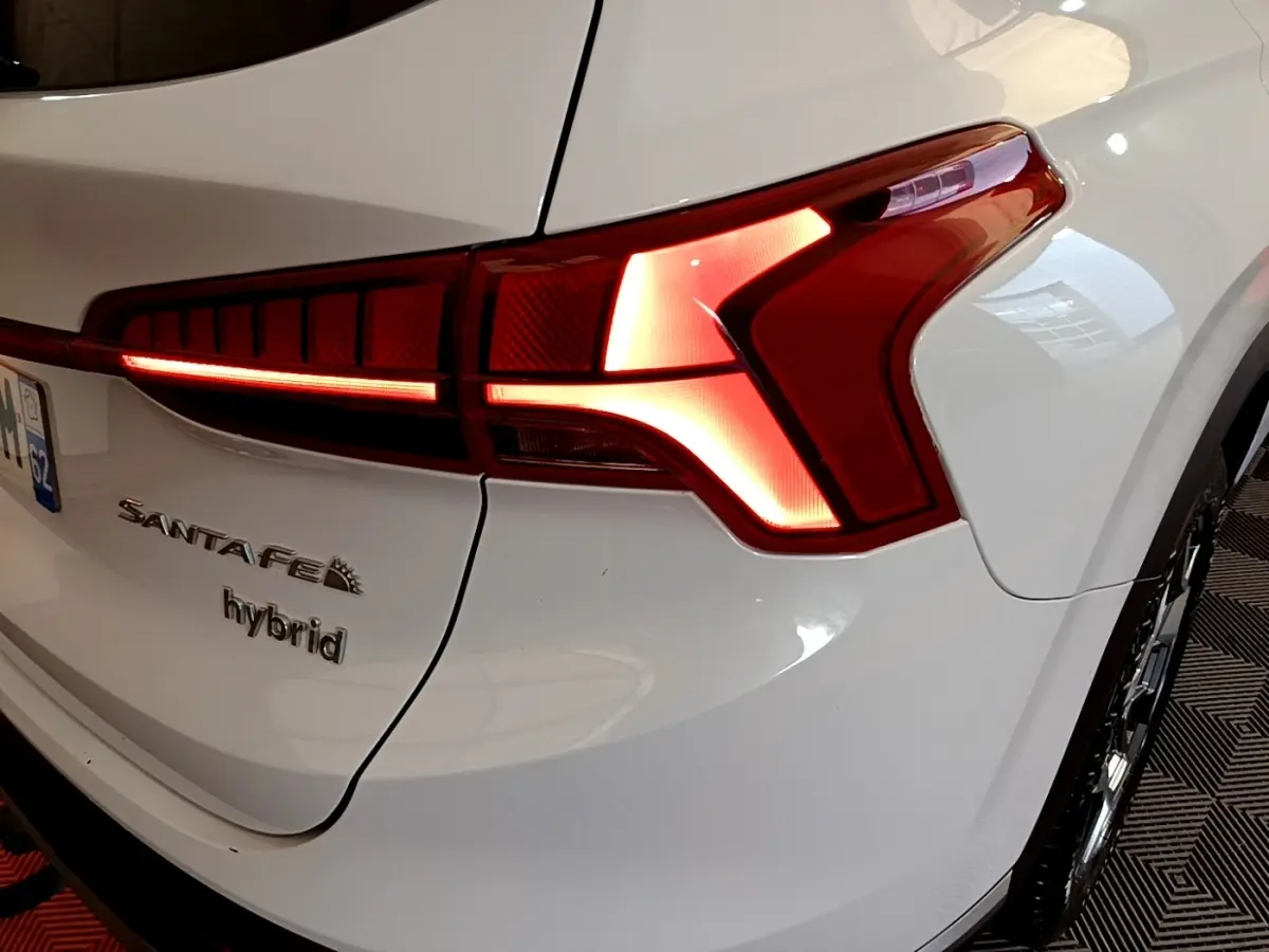 Gros plan sur le feu arrière droit allumé d’un Hyundai Santa Fe blanc hybride avec logo visible sur le coffre.