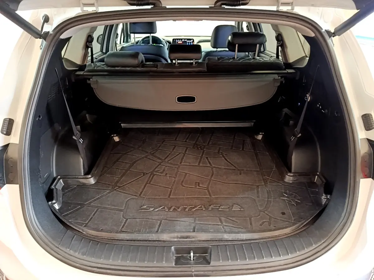 Coffre ouvert d'un Hyundai Santa Fe blanc 2022, vue arrière montrant tapis de coffre et sièges noirs rabattus.