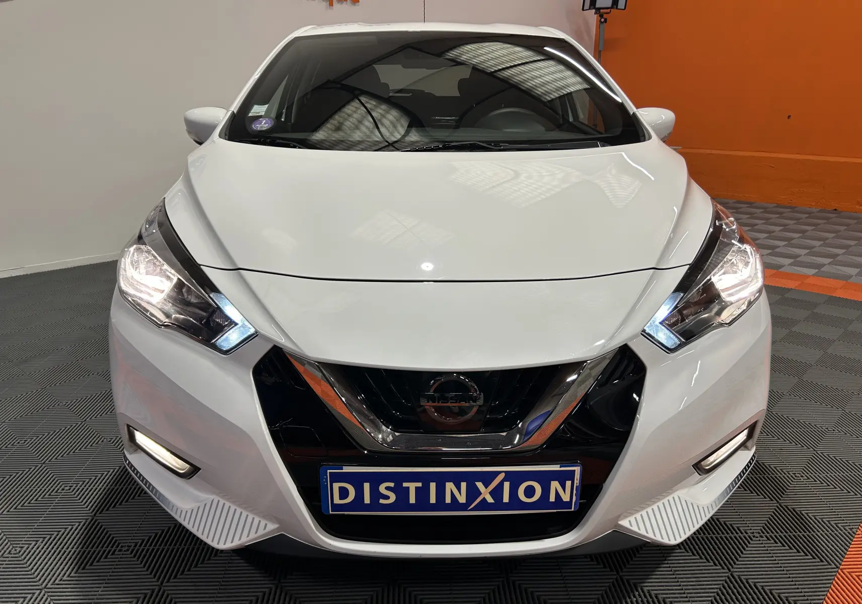 Vue avant d'une Nissan Micra blanche 2021 avec phares allumés et calandre noire brillante dans un showroom.