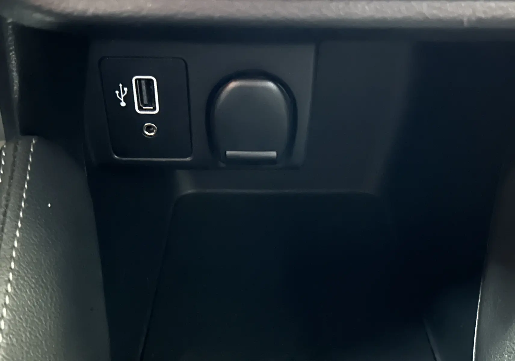 Gros plan sur la prise USB et allume-cigare dans l’espace de rangement central intérieur d’une Nissan Micra blanche.