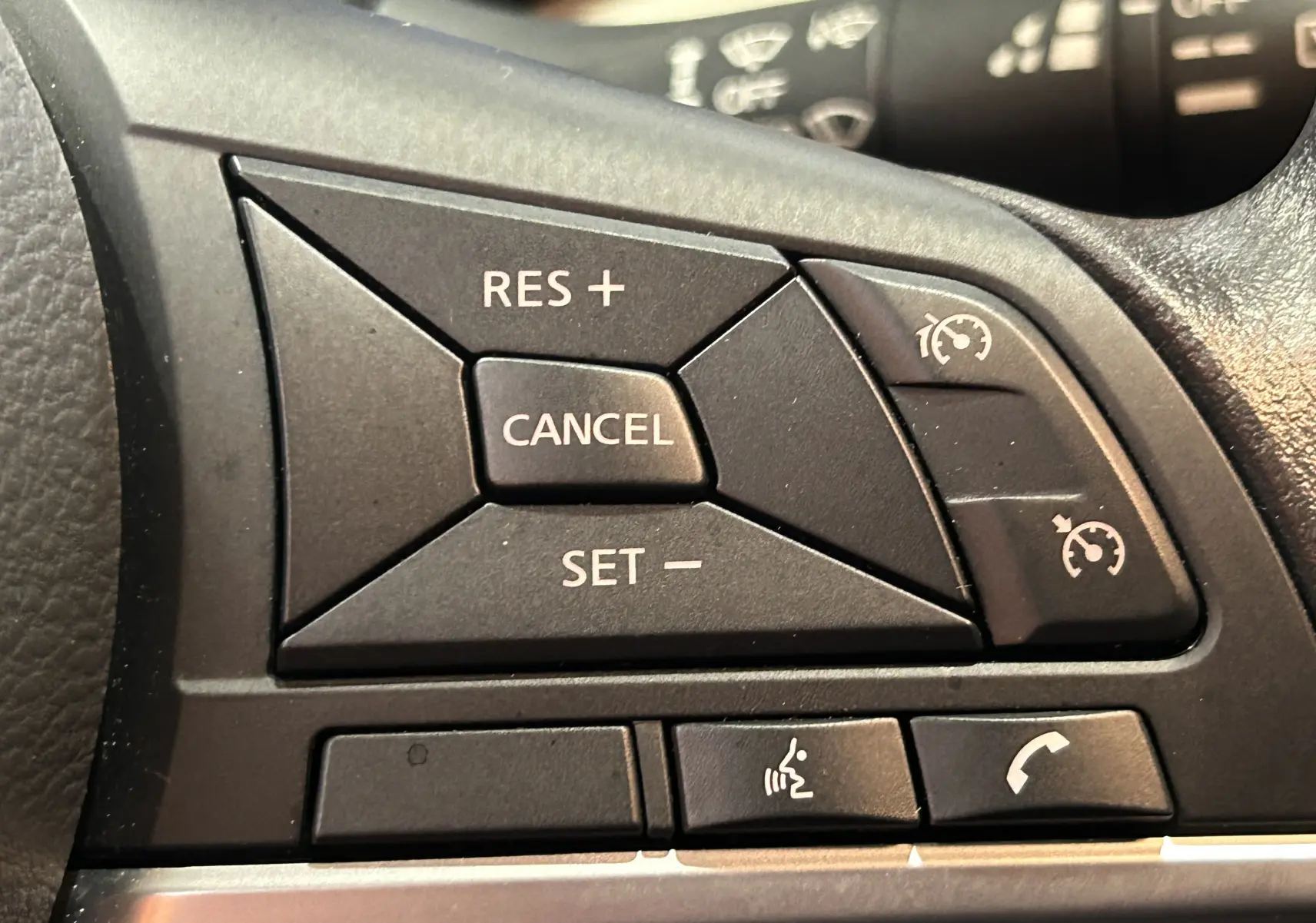 Gros plan sur les commandes de régulateur de vitesse et téléphone au volant d'une Nissan Micra blanche de 2021.