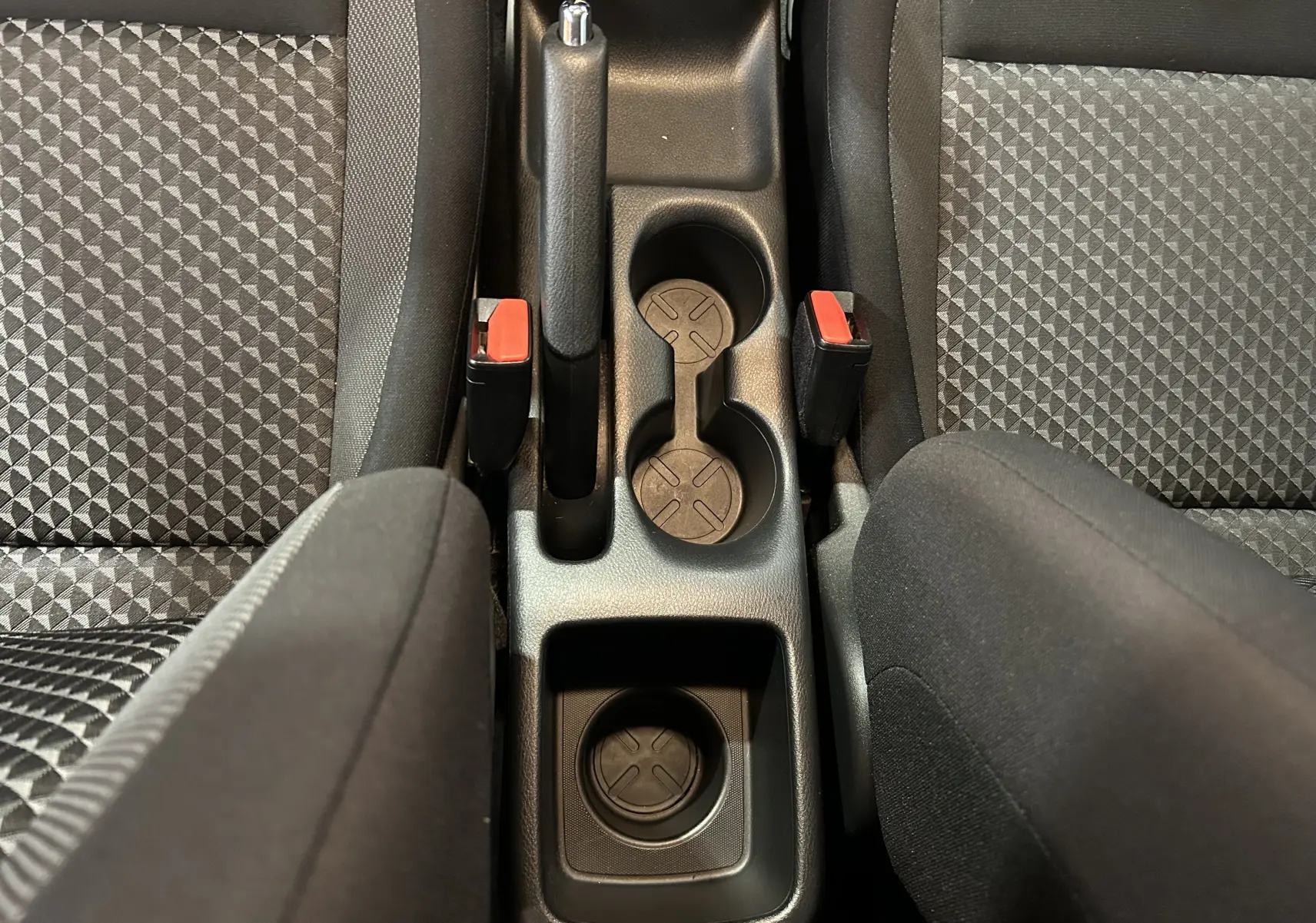 Vue plongeante sur la console centrale noire de la Nissan Micra 2021, avec porte-gobelets et sièges tissu gris à motifs.