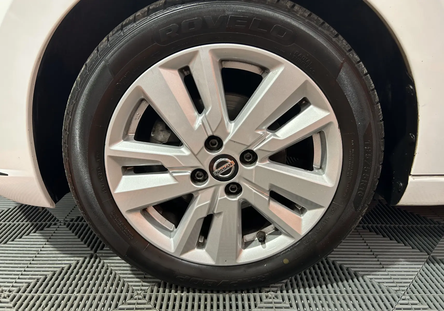 Gros plan sur la roue avant droite d'une Nissan Micra blanche, mettant en valeur la jante en alliage et le logo central.