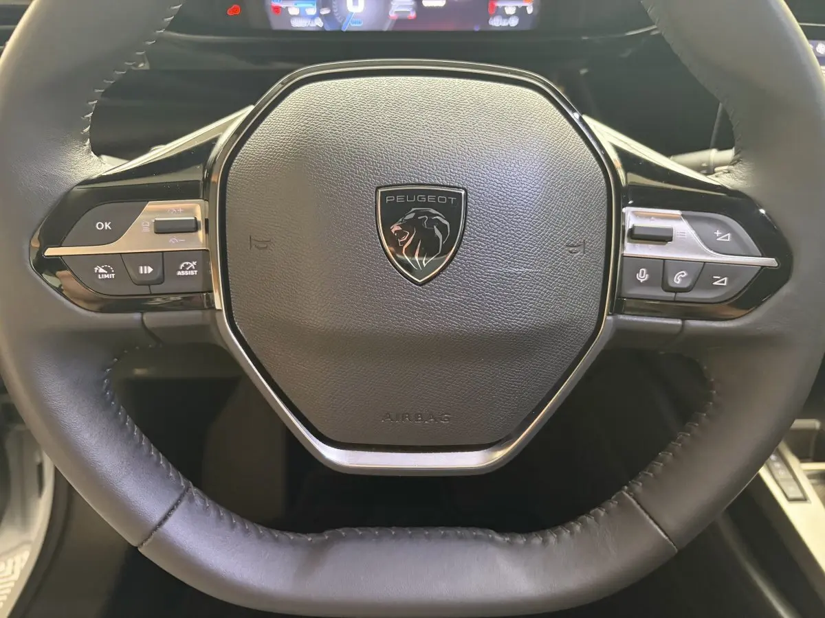 Gros plan sur le volant cuir multifonctions de la Peugeot 308 2024, avec logo lion central et commandes intégrées.