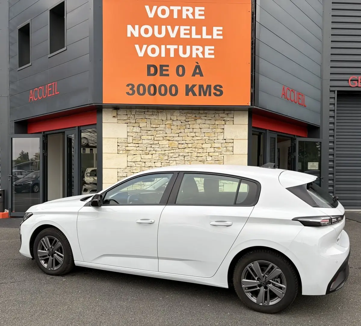 Vue latérale droite d'une Peugeot 308 blanche 2024 garée devant un bâtiment avec panneau orange "Votre nouvelle voiture".