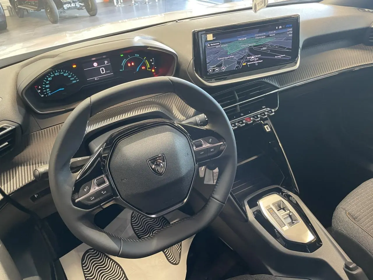 Vue intérieure du poste de conduite du Peugeot 2008 hybride 2026, volant compact noir et écran tactile navigation 10 pouces.