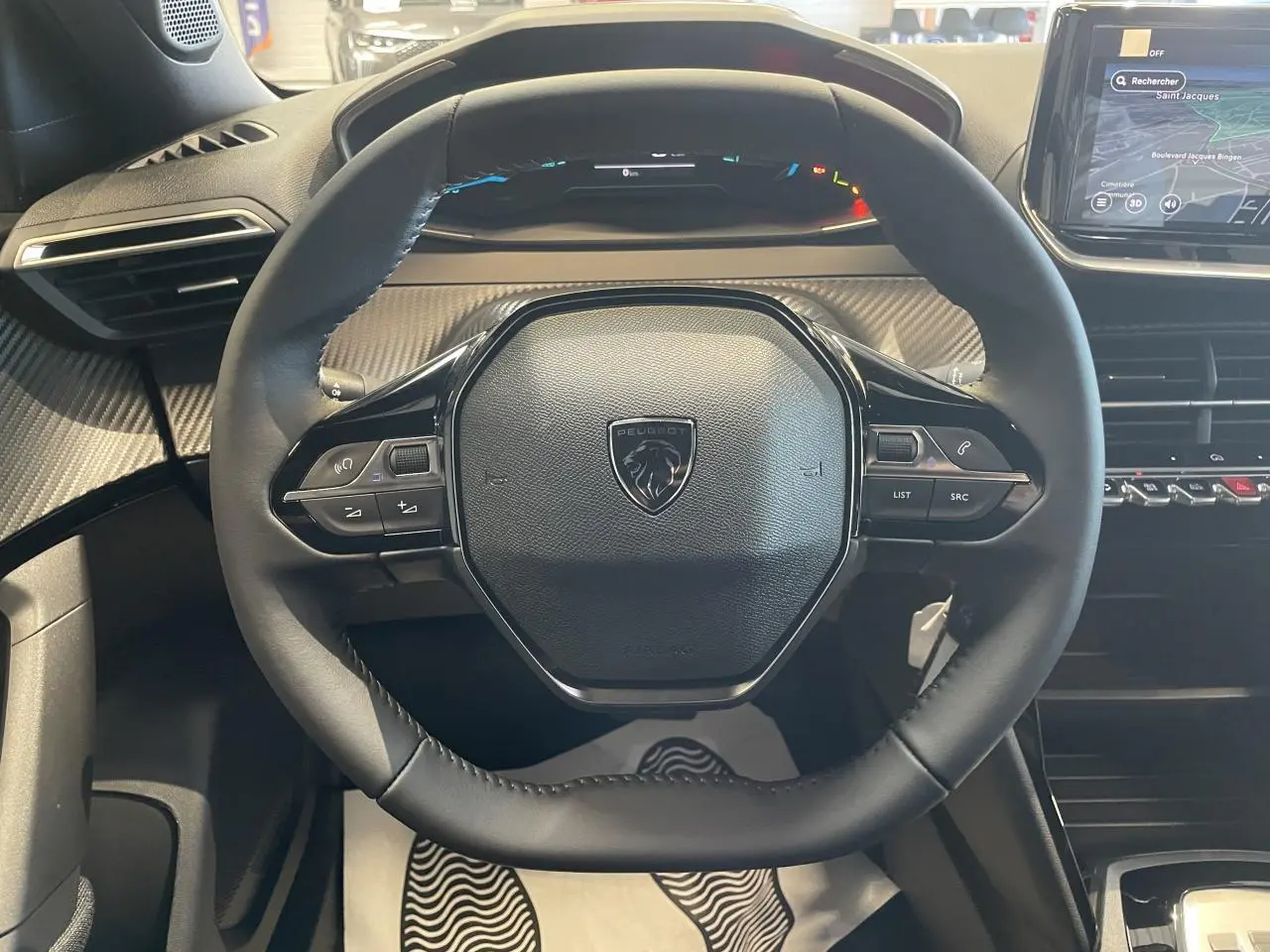 Vue rapprochée du volant compact cuir noir avec commandes intégrées, tableau de bord et écran tactile du Peugeot 2008 hybride 2026.