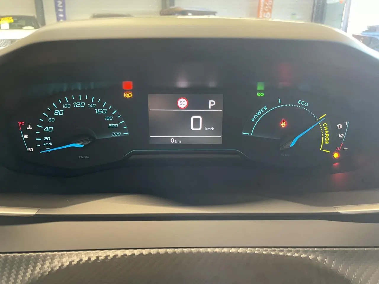 Vue rapprochée du combiné d'instruments numérique du Peugeot 2008 hybride blanc, affichant 0 km/h et indicateurs de charge et vitesse.