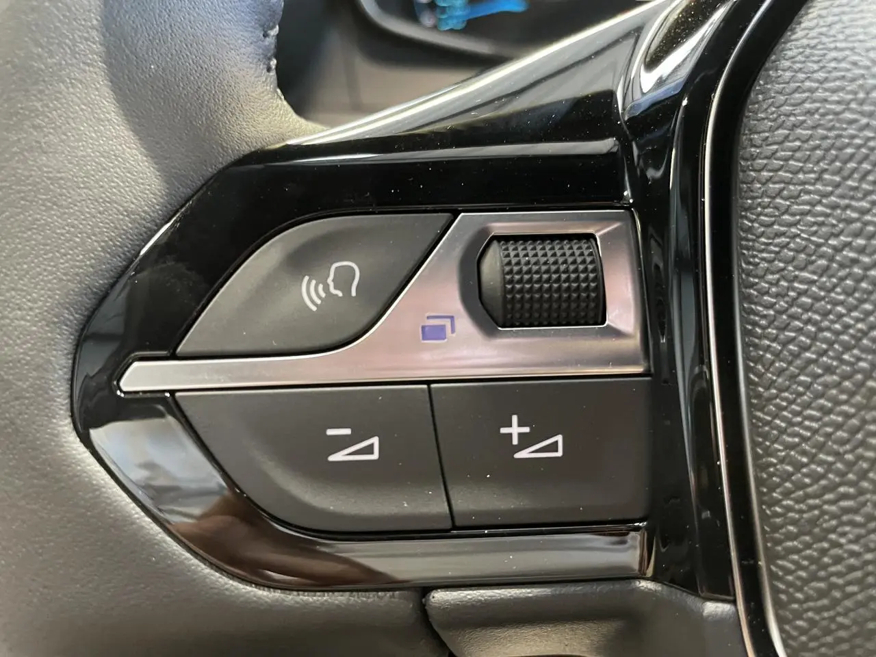Gros plan sur les commandes de volume et reconnaissance vocale sur le volant noir du Peugeot 2008 hybride blanc.