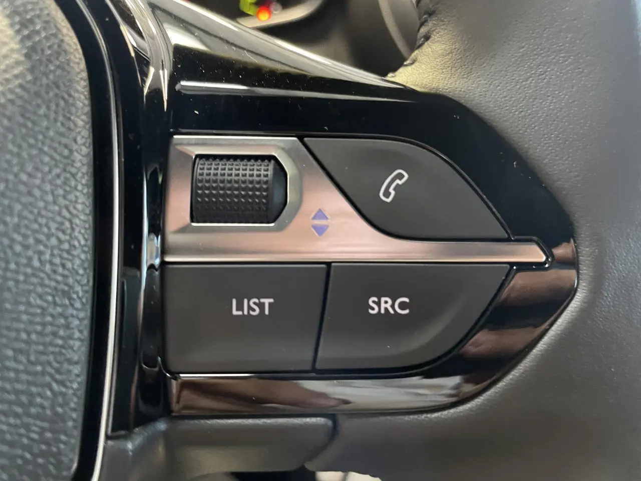 Gros plan sur les commandes multimédia noires du volant cuir du Peugeot 2008 blanc hybride, version 2026.