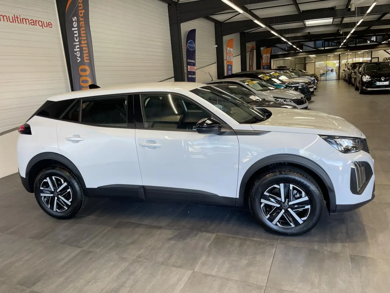 Peugeot 2008 blanc en profil droit dans un showroom, avec jantes noires et détails noirs contrastants.