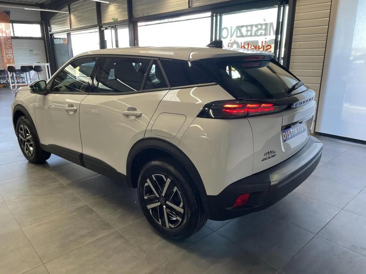 Vue 3/4 arrière droit d'un Peugeot 2008 blanc avec feux arrière LED allumés et jantes alliage noires et argent.
