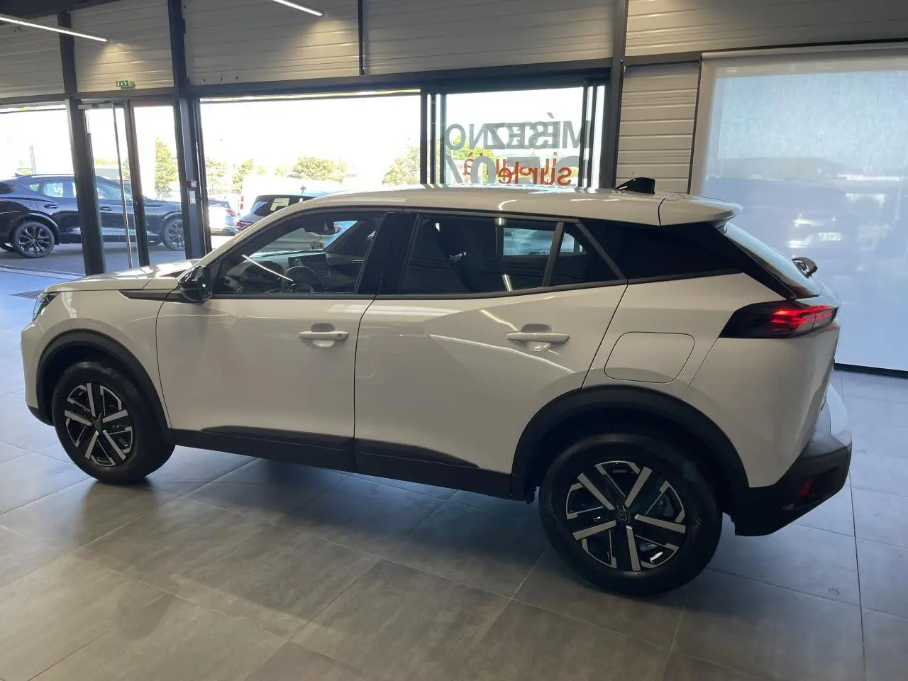 Peugeot 2008 blanc vue de profil côté gauche en intérieur, avec jantes noires et feux arrière LED allumés.