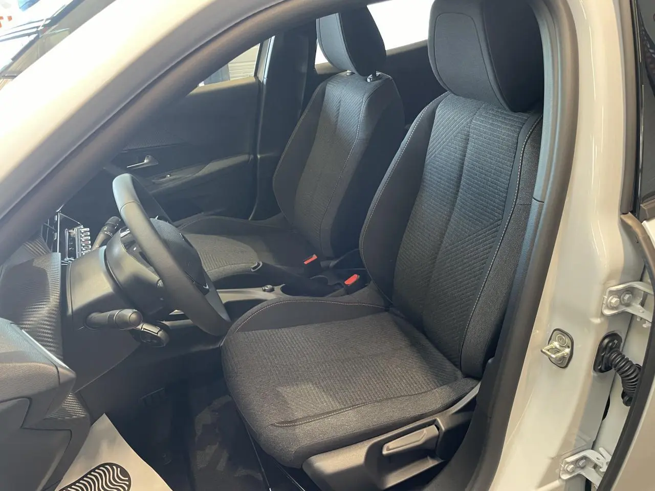 Vue intérieure côté conducteur de la Peugeot 2008 blanche, sièges tissu gris foncé avec surpiqûres contrastantes.