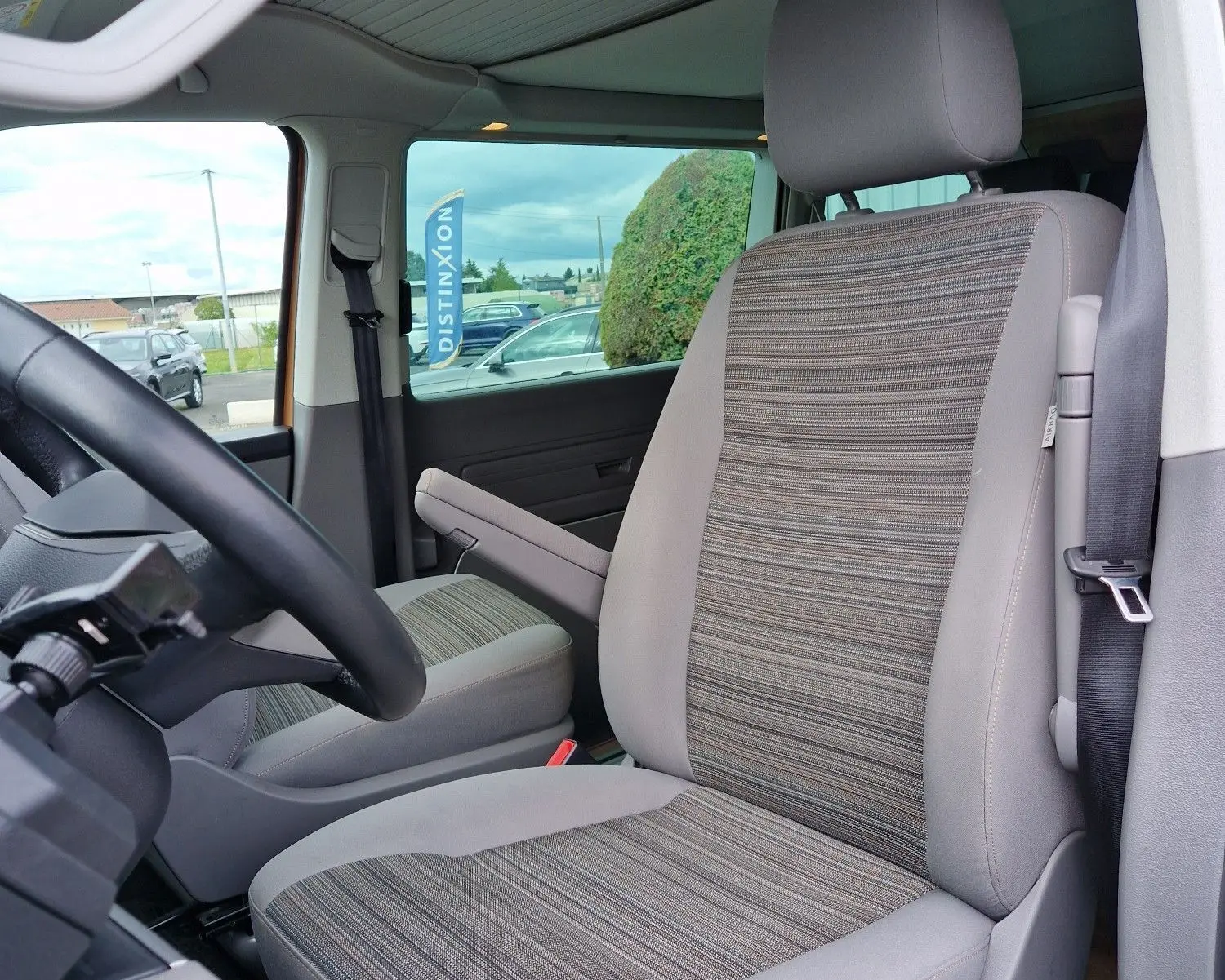 Vue intérieure côté conducteur du Volkswagen California 2021 Cooper bronze, siège avant en tissu rayé gris et beige.