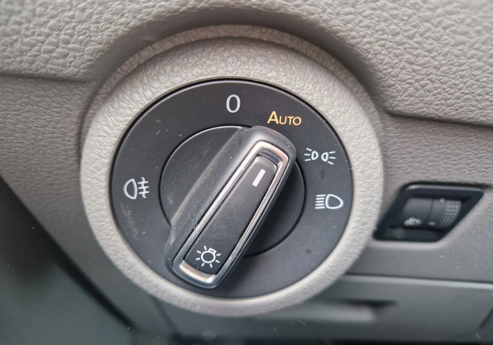 Gros plan sur le sélecteur de phares du Volkswagen California 2021, avec molette en position automatique sur tableau de bord gris.