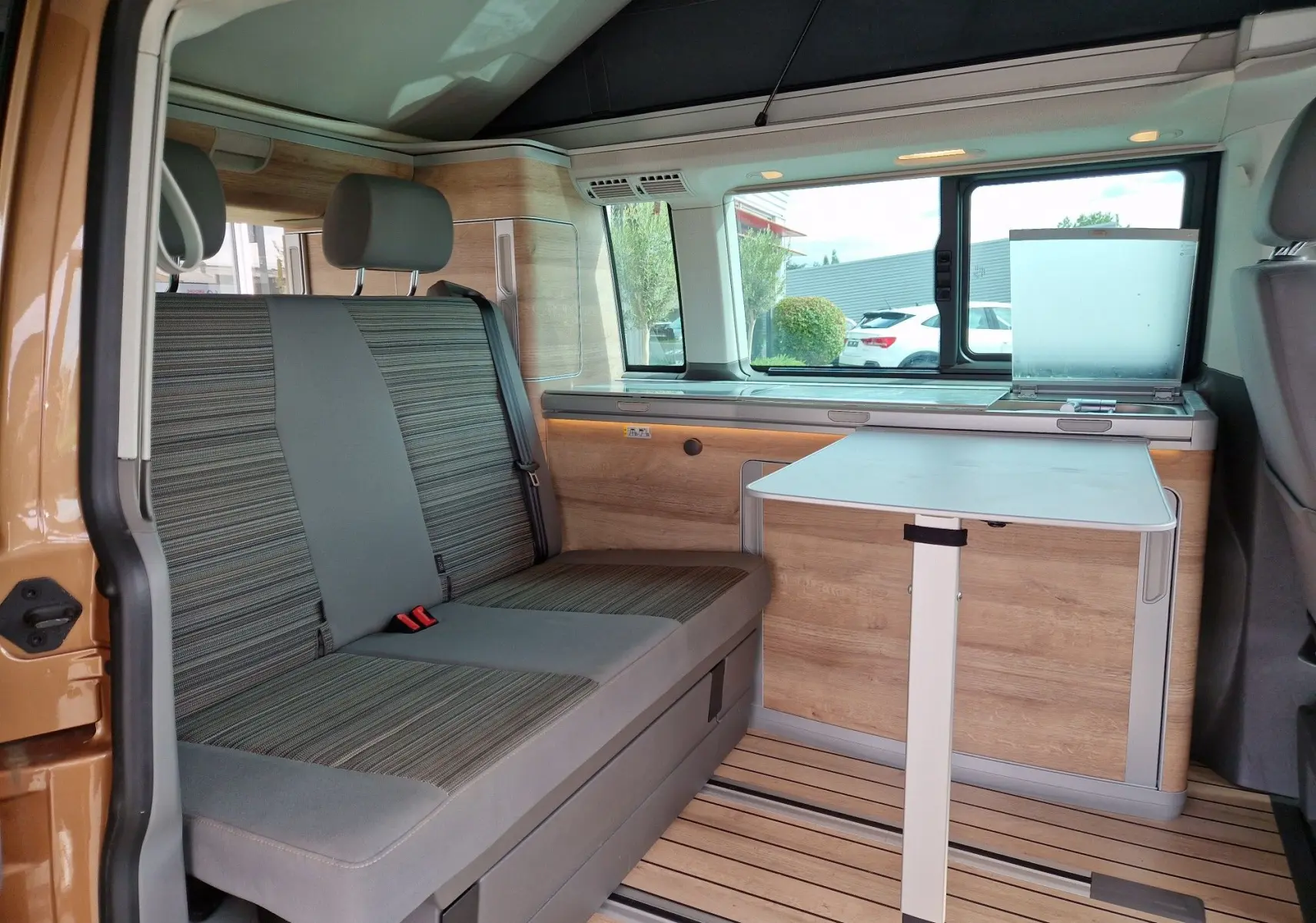 Intérieur du Volkswagen California Cooper bronze 2021, vue côté gauche sur banquette et table pliante en bois clair.