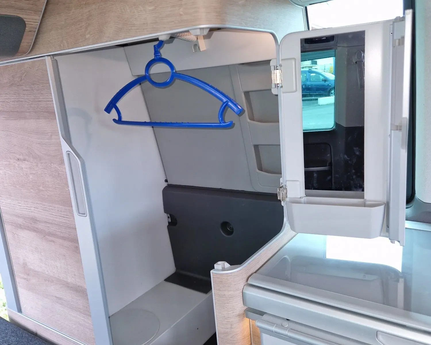 Intérieur du Volkswagen California 2021 en Cooper bronze, vue sur le placard ouvert avec un cintre bleu et un miroir rabattable.