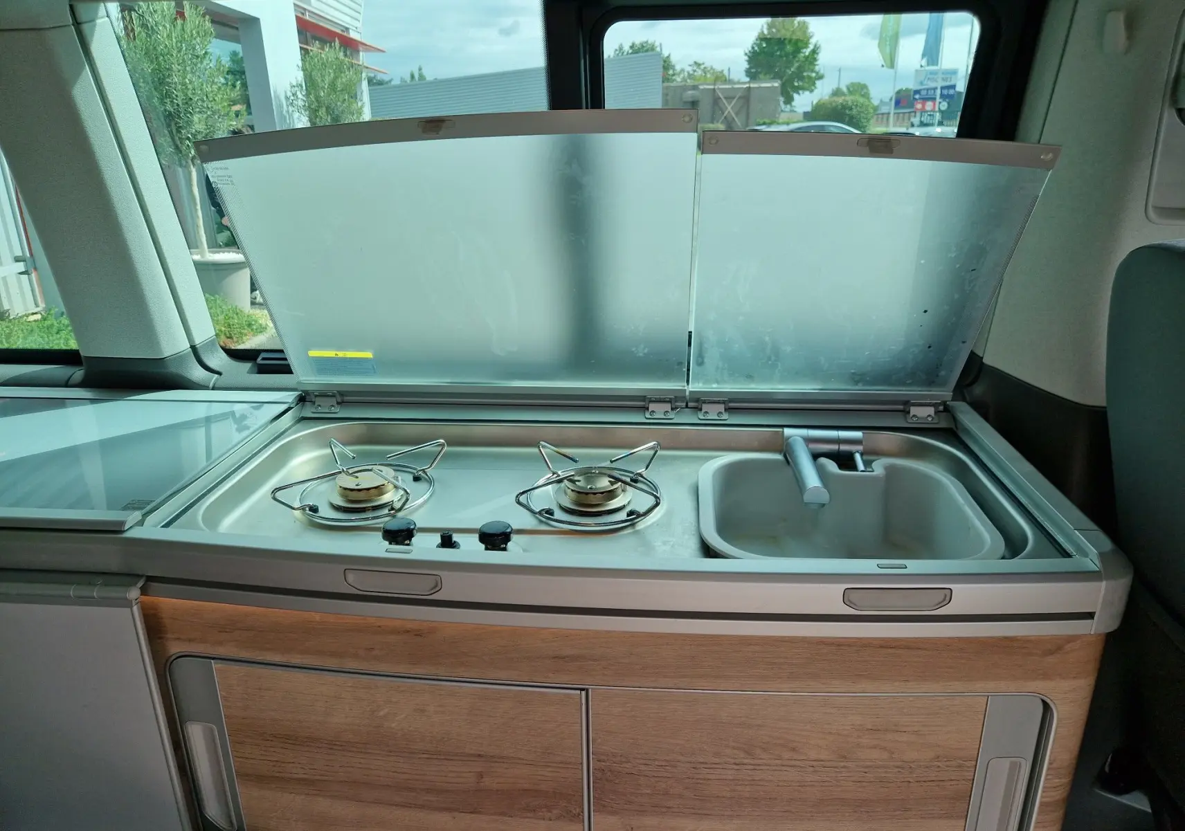 Cuisine intégrée avec deux feux gaz et évier dans un Volkswagen California Cooper bronze, vue intérieure côté droit.