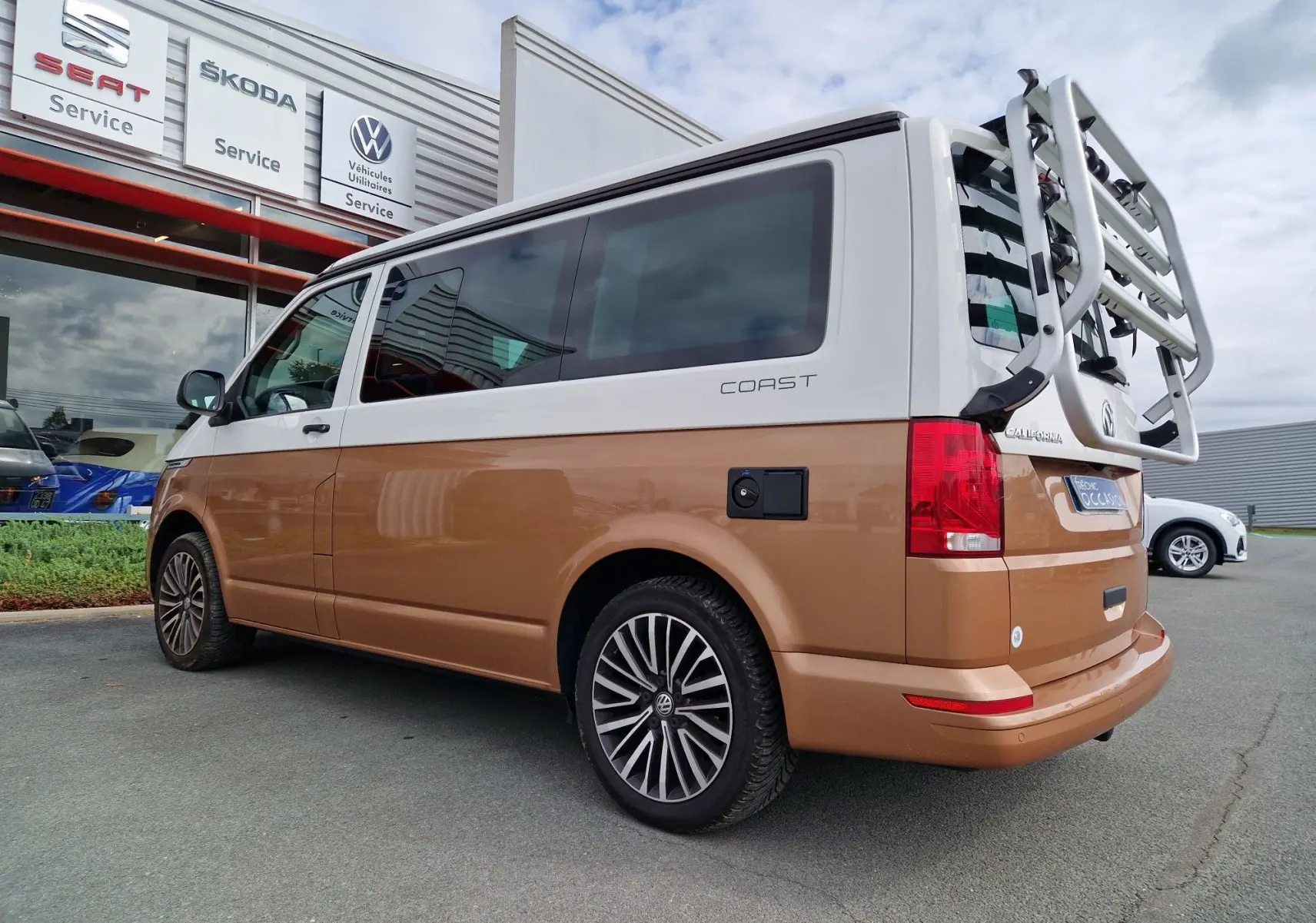 Vue 3/4 arrière droite du Volkswagen California Coast 2021 en Cooper bronze avec porte-vélos fixé au hayon.