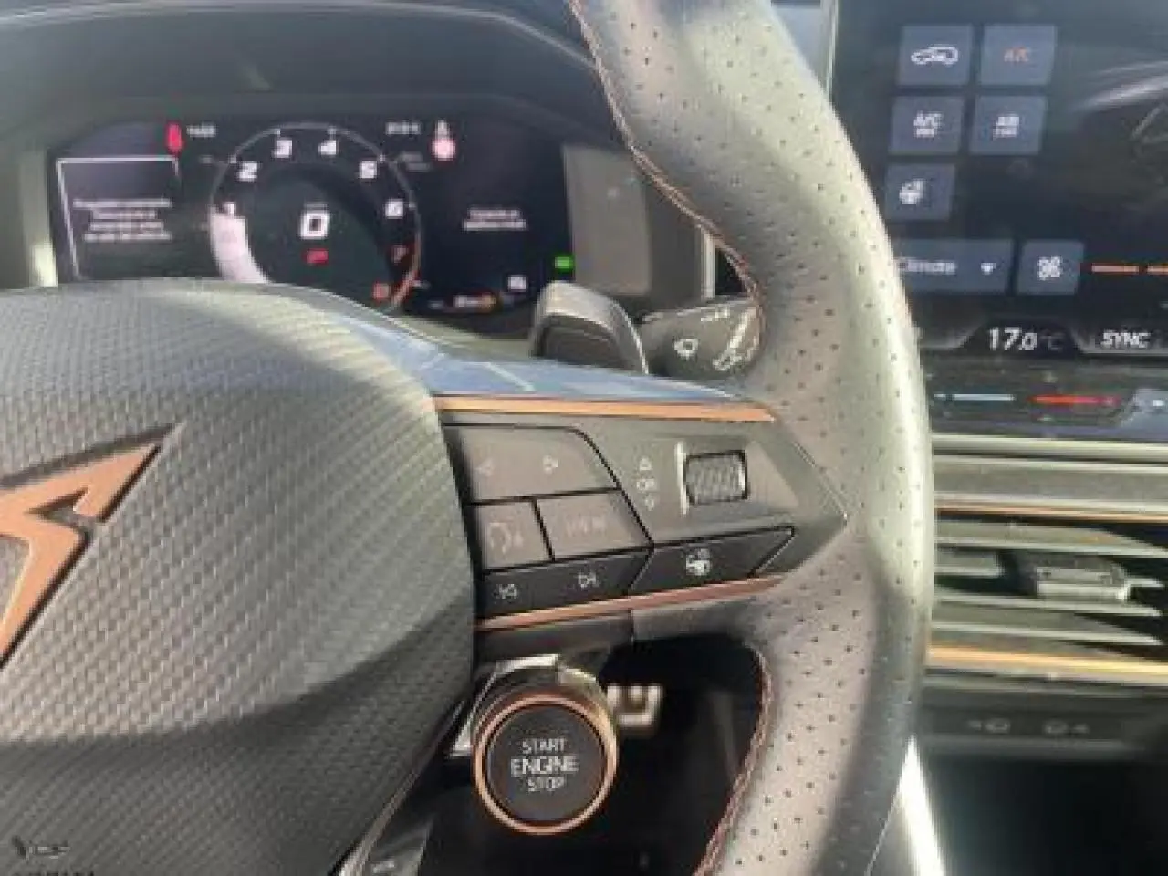 Gros plan sur le volant en cuir perforé avec logo CUPRA et bouton start/stop, tableau de bord digital en arrière-plan.