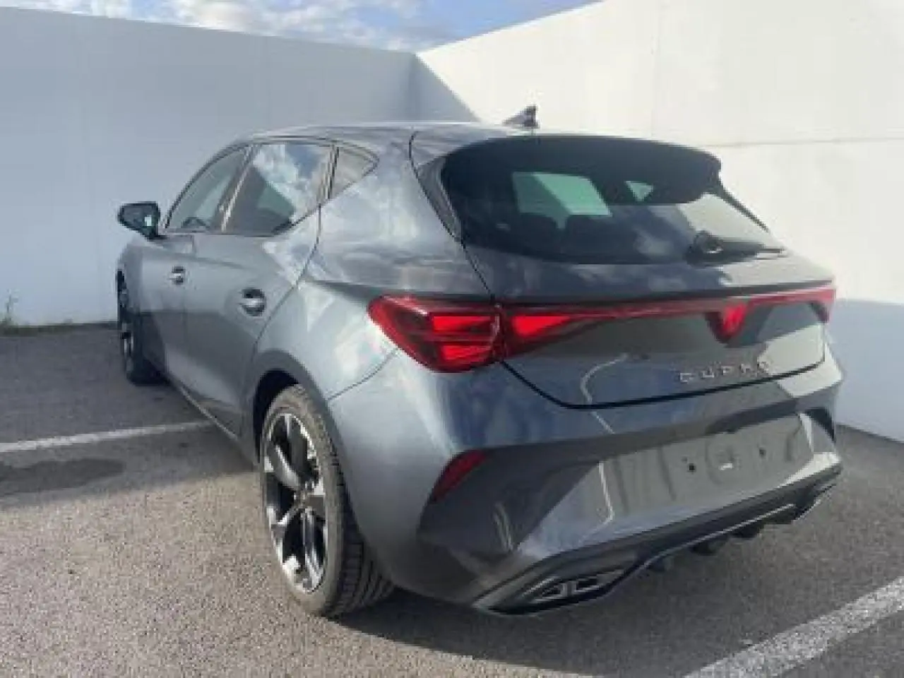 Vue 3/4 arrière droite d'une CUPRA Leon 2025 gris magnetic metal avec bandeau lumineux arrière et jantes alliage noires.