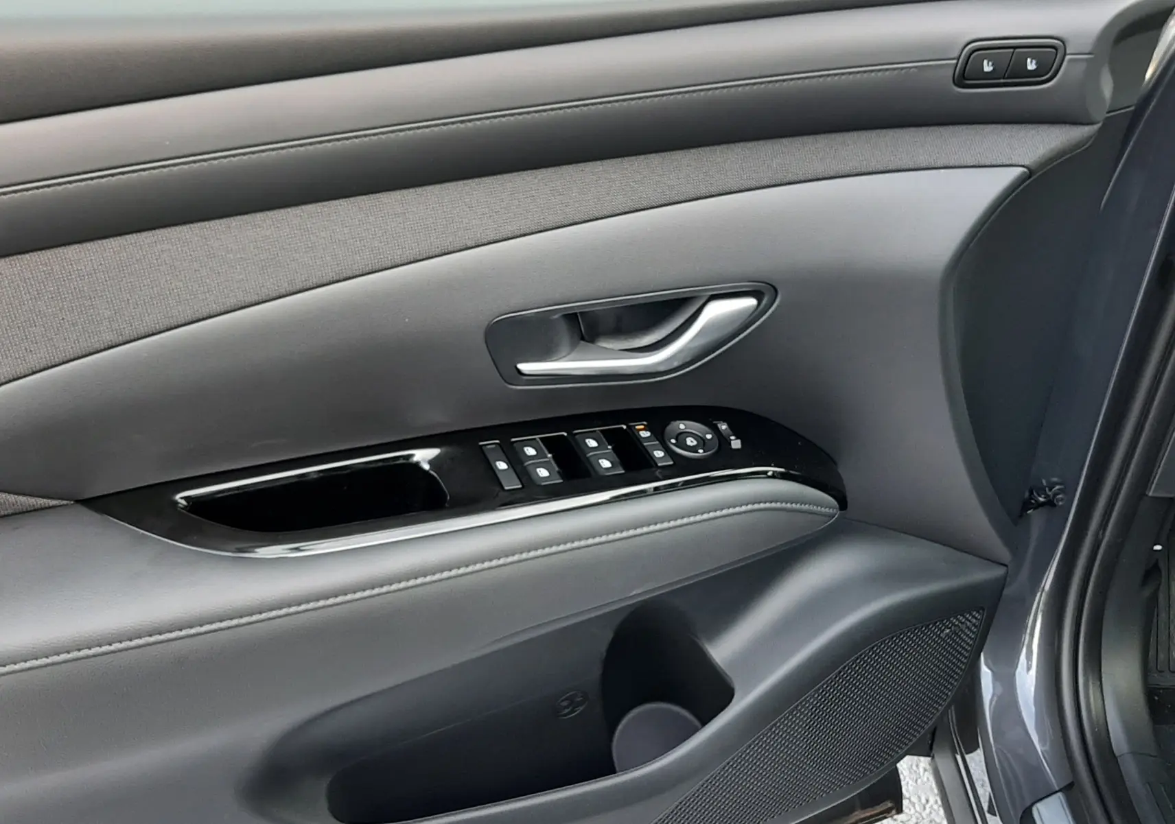 Intérieur côté gauche de la porte avant d'un Hyundai Tucson gris, avec commandes électriques et habillage noir.