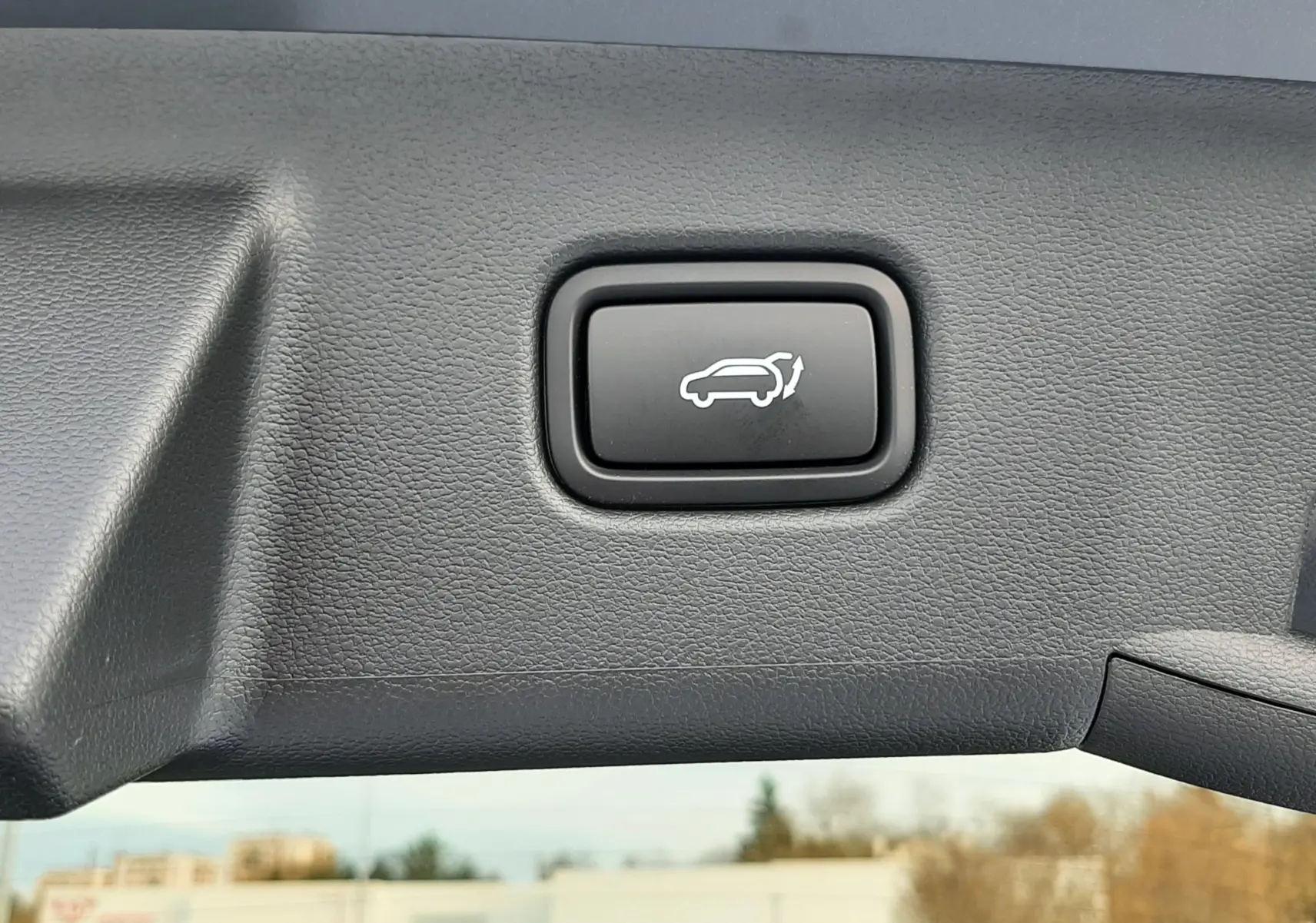 Bouton noir d'ouverture électrique du hayon sur le bord intérieur du coffre du Hyundai Tucson gris Ecotronic.
