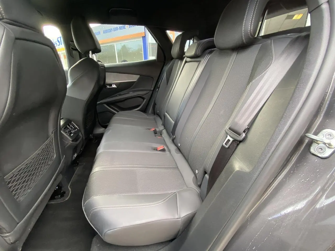 Vue côté droit des sièges arrière en cuir gris foncé du Peugeot 3008 2023, avec ceintures et filet de rangement au dos des sièges avant.