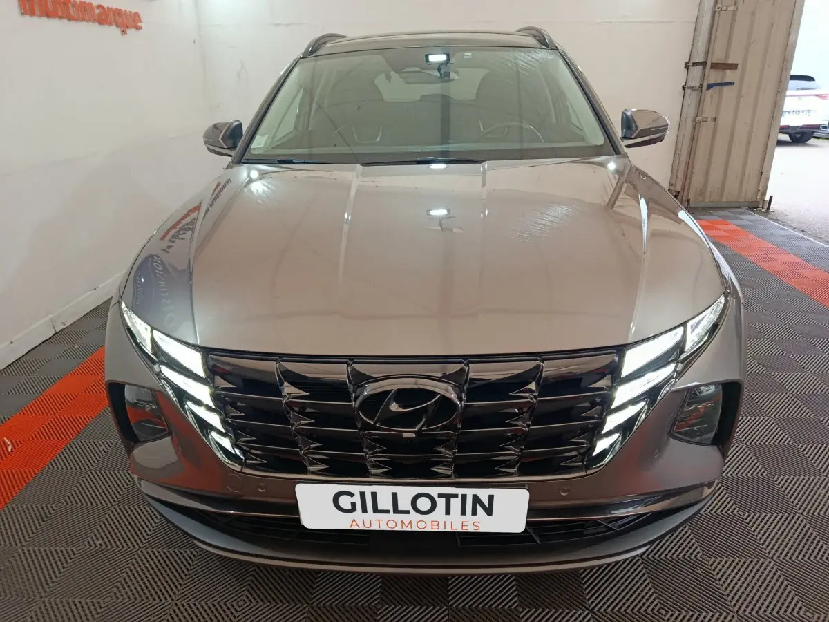 Vue avant d'un Hyundai Tucson marron 2022 avec calandre noire et phares LED allumés en intérieur showroom.