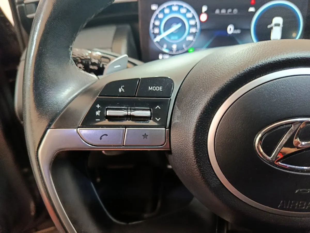 Gros plan sur le côté gauche du volant noir du Hyundai Tucson 2022 avec commandes audio et logo Hyundai visible.