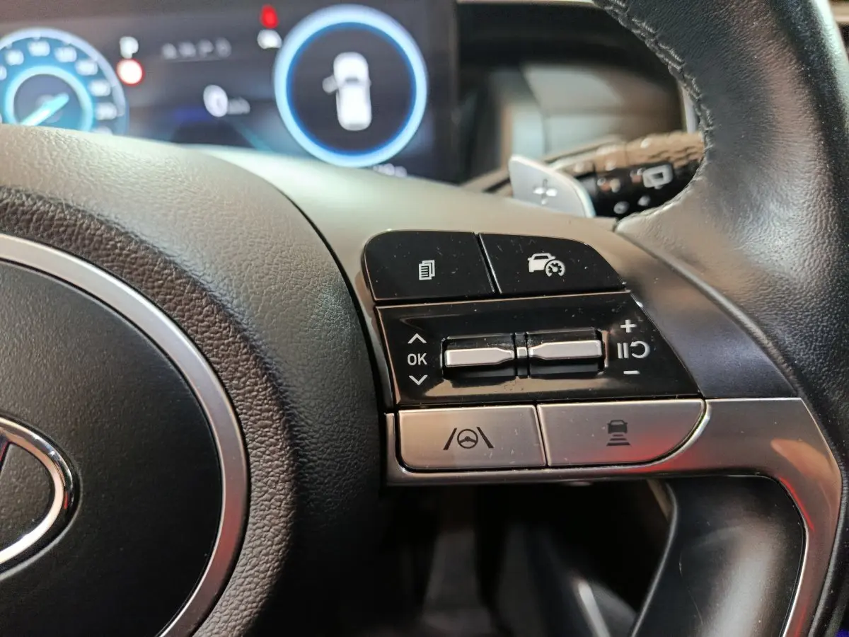 Gros plan sur les commandes à droite du volant cuir du Hyundai Tucson marron, avec affichage digital en arrière-plan.