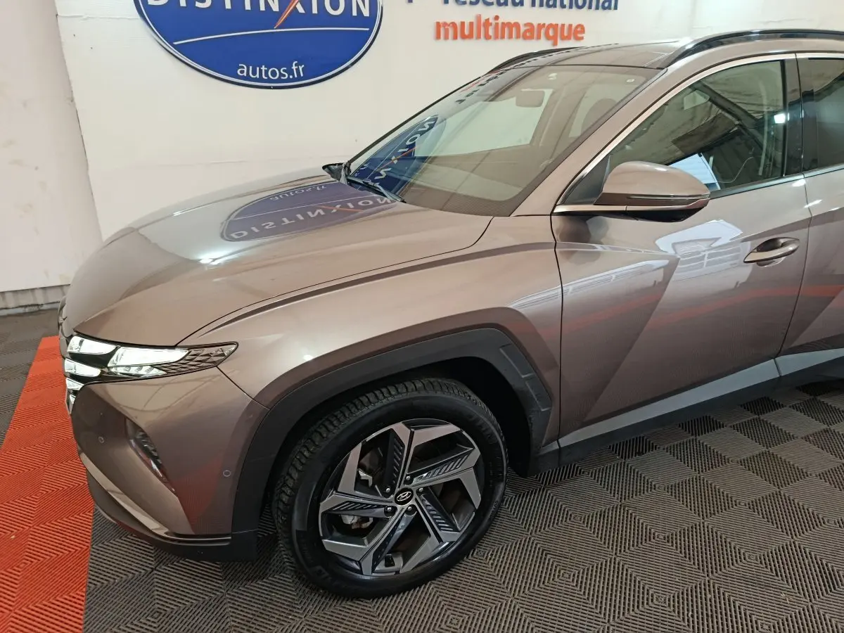 Vue 3/4 avant droit d'un Hyundai Tucson marron avec jantes alliage et feux LED distinctifs en intérieur showroom.