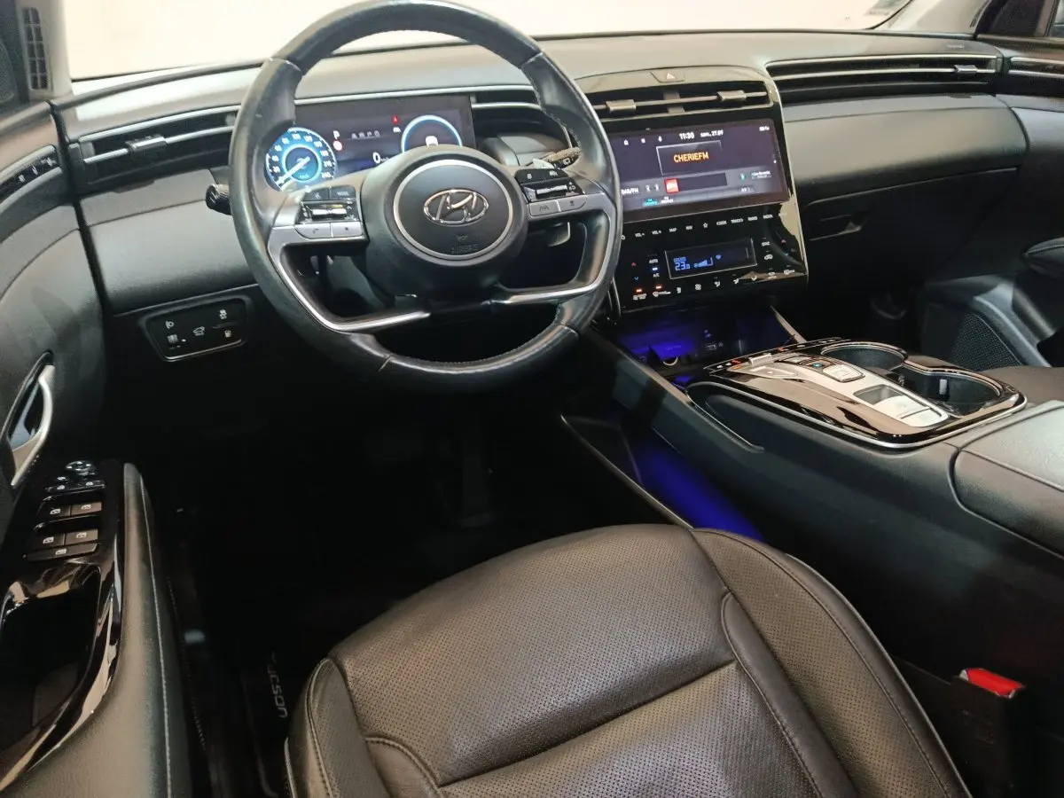 Intérieur noir du Hyundai Tucson 2022, vue côté conducteur sur volant cuir, tableau de bord digital et console centrale brillante.