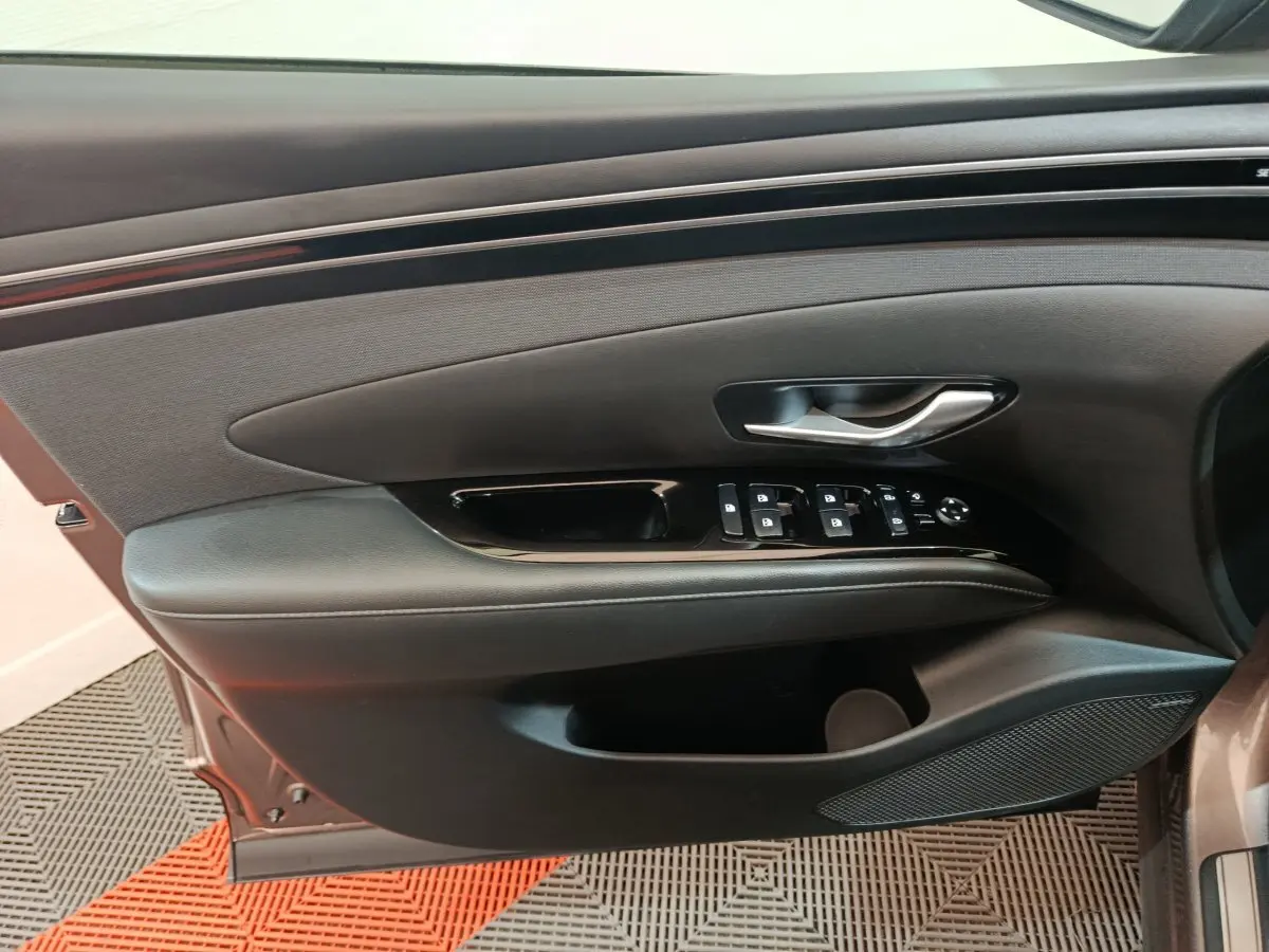 Vue rapprochée de la porte avant gauche marron du Hyundai Tucson 2022, avec commandes électriques et poignée argentée.