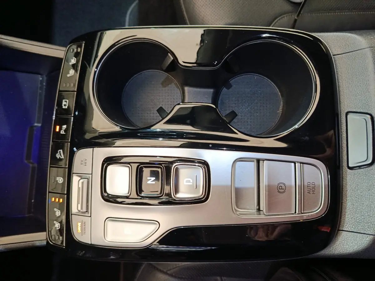 Vue plongeante sur la console centrale noire brillante du Hyundai Tucson marron 2022 avec commandes de boîte auto et porte-gobelets.