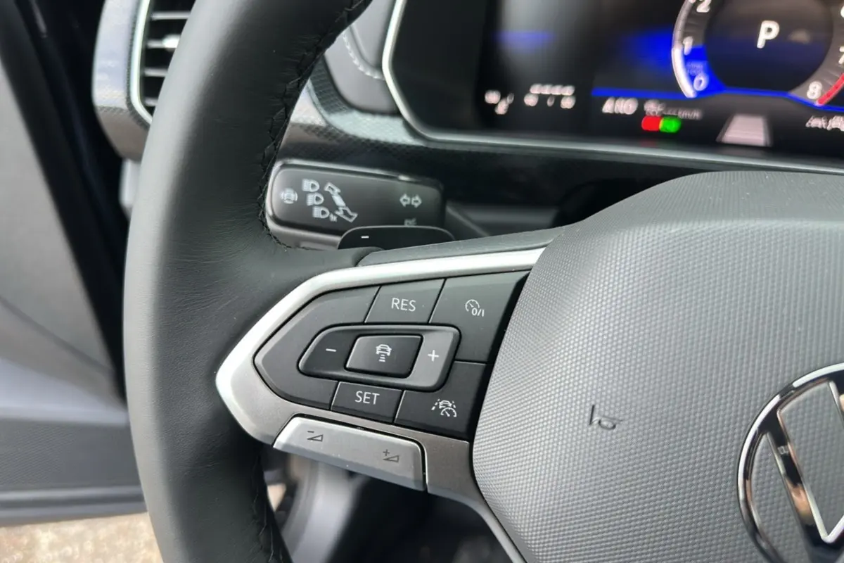 Gros plan sur le volant cuir noir du Volkswagen T-Cross 2025, avec commandes multifonctions et tableau de bord digital visible.