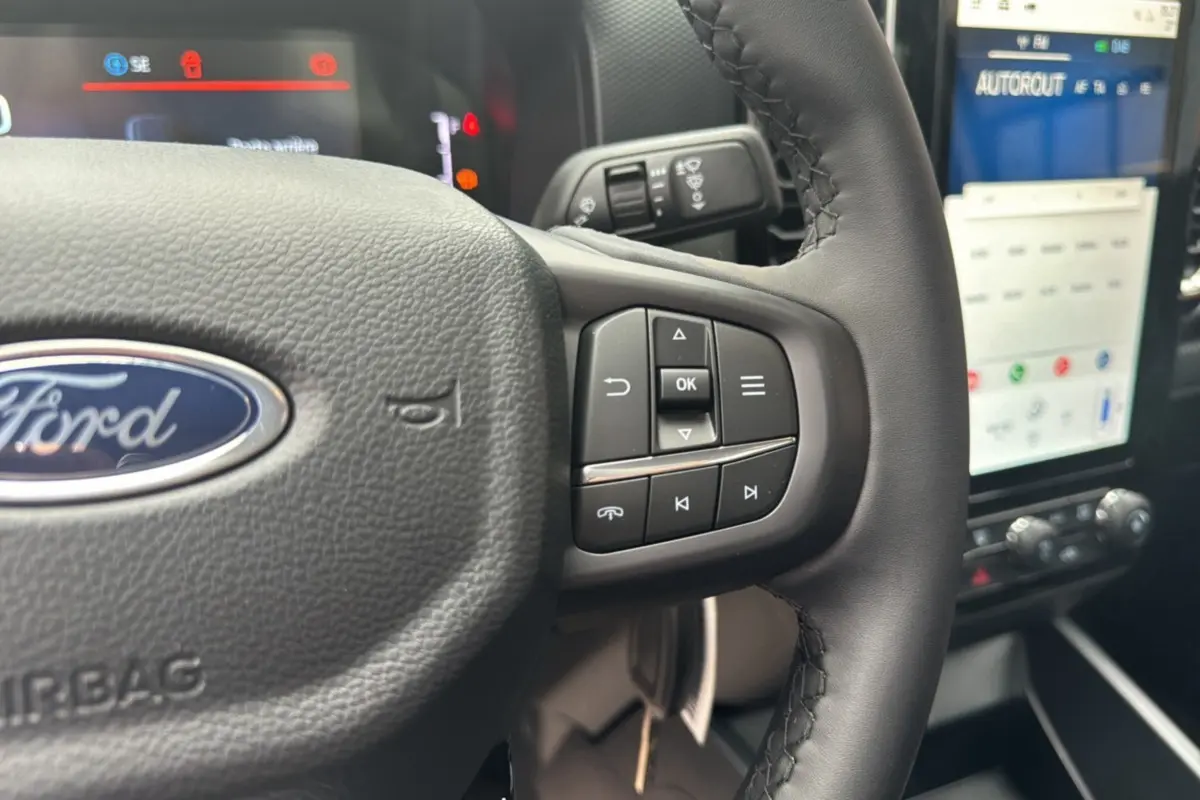 Gros plan sur le volant cuir multifonctions du Ford Ranger avec commandes intégrées et écran tactile en arrière-plan.